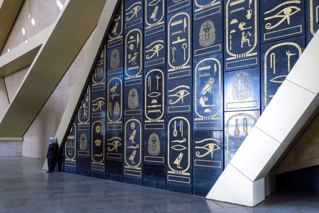 Golden Royal Cartouche and hieroglyphics on a black wall at the Grand Egyptian Museum, showcasing ancient Egyptian art.
