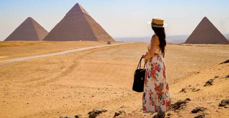 Alt Text: Woman in floral dress viewing Giza Pyramids tour landscape, standing in the desert under a clear sky with ancient monuments.