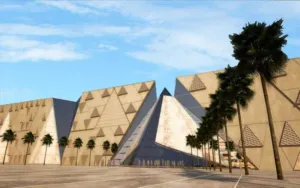 Grand Egyptian Museum facade featuring modern pyramidal architecture and palm trees under a blue sky in Giza.
