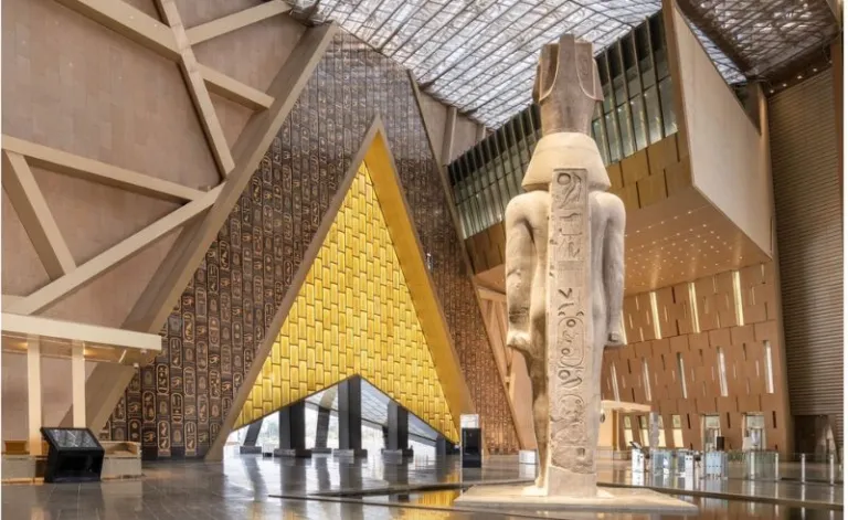 Statue of Ramses II in the Grand Egyptian Museum atrium, featuring a hieroglyphic wall and modern architectural design.