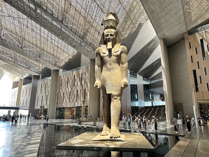 Back view of Ramses II statue facing a golden triangular wall with hieroglyphs during a grand-egyptian-museum-tour.