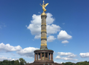 Golden Victoria statue atop Victory Column in Berlin under a blue sky with white clouds, showcasing historic architecture.