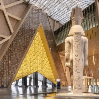 Statue of Ramses II in the Grand Egyptian Museum atrium, featuring a hieroglyphic wall and modern architectural design.