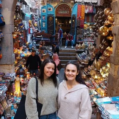 Two tourists in Khan el-Khalili market, Cairo, surrounded by traditional lanterns, colorful crafts, and historic architecture.